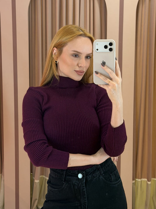 Modelo vestindo blusa cacharrel feminina em tricô canelado roxo com gola alta e manga longa, combinada com calça preta.