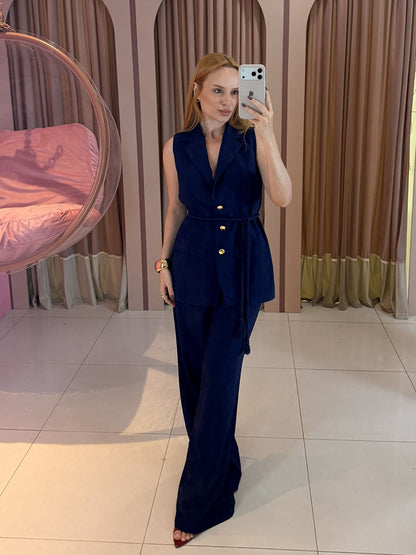 Modelo vestindo conjunto feminino Marrant com colete alongado sem mangas, faixa para amarração na cintura e calça pantalona de alfaiataria azul marinho.