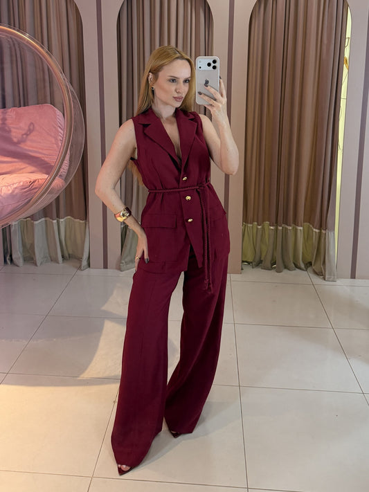 Modelo vestindo conjunto feminino Marrant com colete alongado sem mangas, faixa para amarração na cintura e calça pantalona de alfaiataria vinho.