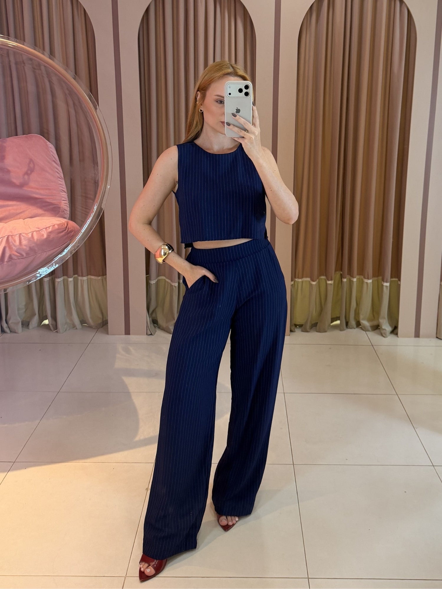Modelo vestindo conjunto feminino risca de giz azul marinho composto por cropped sem mangas e calça pantalona de cintura alta.