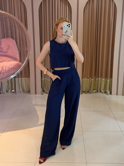 Modelo vestindo conjunto feminino risca de giz azul marinho composto por cropped sem mangas e calça pantalona de cintura alta.