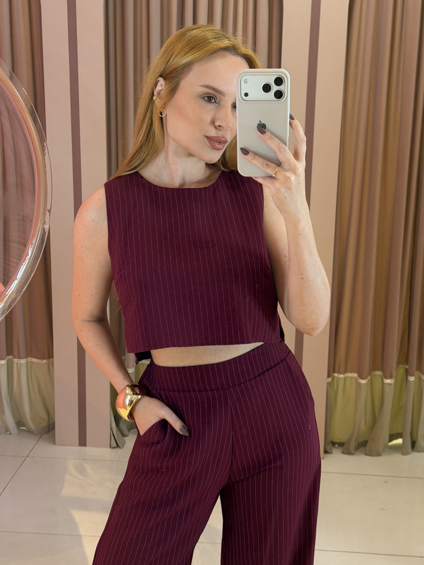 Modelo vestindo conjunto feminino risca de giz marsala composto por cropped sem mangas e calça pantalona de cintura alta.
