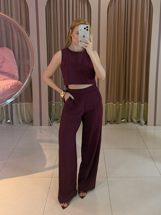 Modelo vestindo conjunto feminino risca de giz marsala composto por cropped sem mangas e calça pantalona de cintura alta.